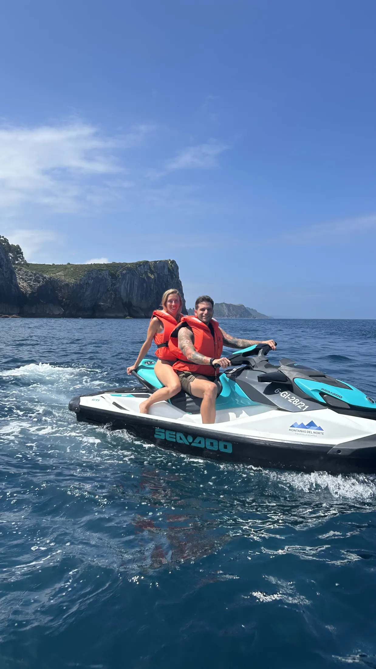 Tú y yo en una moto de agua, con un acantilado y el cielo azul detrás.