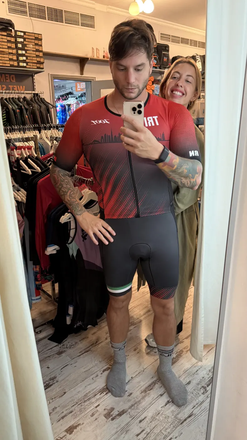 Yo probándome un traje de triatlón frente al espejo; tú asomas detrás, sonriendo.